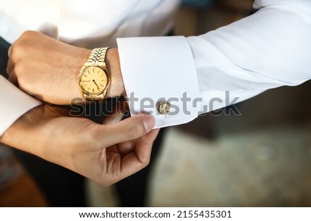The groom fastens his cufflink at the wedding gathering. Royalty-Free Stock Photo #2155435301