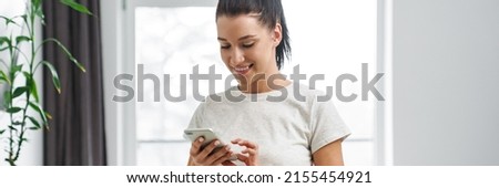 European smiling woman using mobile phone and making salad in kitchen at home