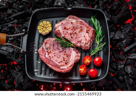Raw steak with vegetables and herbs on a grill pan. On burning charcoal barbeque. Organic meat