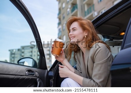 Shot of adult woman sitting in her car with open door, contemplating and sipping coffee from a travel mug. Royalty-Free Stock Photo #2155478111