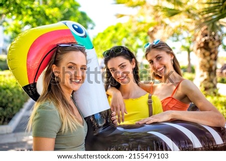 group of beautiful women portrait on summer vacation holiday carrying inflatable toucan mattress on the street having fun together hugging each other. friends travel journey walking. lifestyle concept