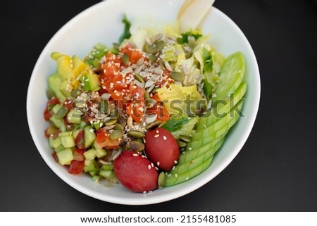 Salmon fresh vegetable salad of tomato, avocado, cucumber, lettuce and spinach. Healthy and detox food concept. Ketogenic diet. Buddha bowl dish on black background, top view.