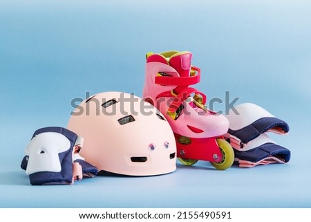 Set of roller skates and protective gear set - knee, elbow and wrist pads and helmet in pink colors. Blue background flat lay 