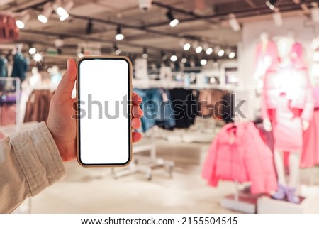 A girl holds a phone in her hand with a blank isolated screen on the background of a blurred shopping center.
