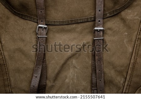 Close-up texture of a canvas fabric backpack. Leather straps and metal buckles. Vintage khaki background.