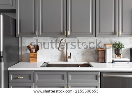 A kitchen sink detail shot with grey cabinets, a white marble countertop and backsplash, and decorations. Royalty-Free Stock Photo #2155508653