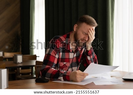 frustrated young man reading documents and using laptop in cafe, money problem, debt notification, bad financial report, unsuccessful exam or test results, business failure concept Royalty-Free Stock Photo #2155551637