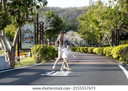 Young mother and son cross the road in the park.