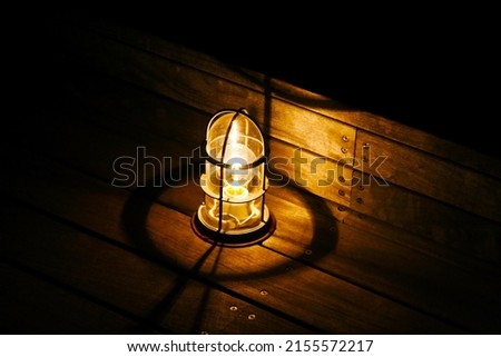 Amber lit lamp on the wooden deck of the harbor side, image processed photo illustration.
