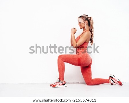 Fitness smiling woman in pink sports clothing. Young beautiful model with perfect body.Sexy female posing in studio near white wall. Doing forward lunges. Stretching out before training Royalty-Free Stock Photo #2155574811