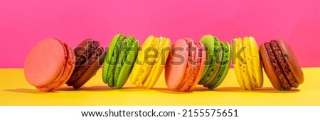 Bright colorful (yellow, pink, green, brown) various flavor macarons sweet cookies on high-colored pink yellow background.  Stack of small french macaron cakes, copy space flatlay 
