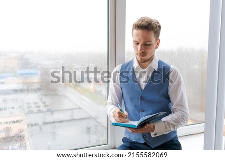 Casual businessman with pen in writing on paper notebook in office in shirt and vest. Student taking note on notepad. Makes plans for successful work, thinks over a business strategy Royalty-Free Stock Photo #2155582069