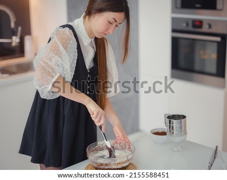 DIY home cooking concept. brunette woman sifting flour for cake through sieve, salting dough. Young woman smiling, loves to cook in beautiful modern kitchen.