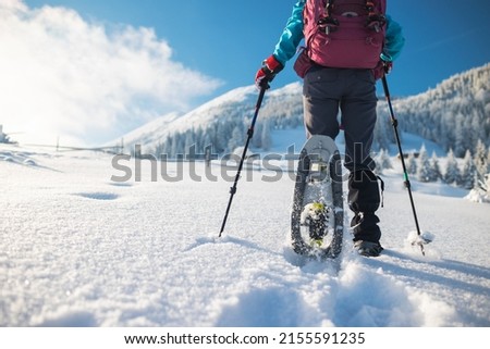 a woman with a backpack in snowshoes climbs a snowy mountain, winter trekking, hiking equipment