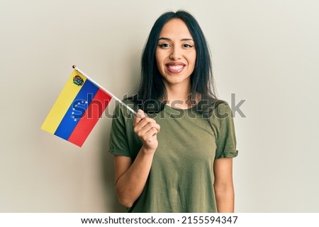 Young hispanic girl holding venezuelan flag looking positive and happy standing and smiling with a confident smile showing teeth 