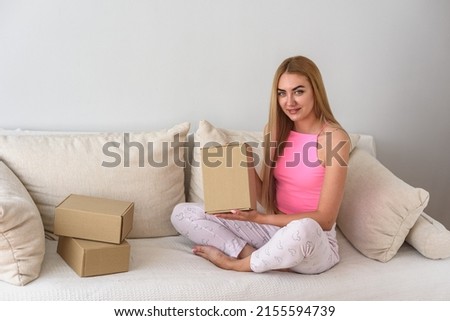 The blonde sits at home on the couch and holds a cardboard box in her hands. The girl holds a box in her hands with the flat side facing the camera.