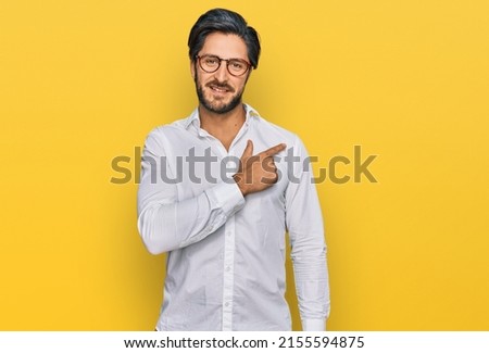 Young hispanic man wearing business shirt and glasses cheerful with a smile of face pointing with hand and finger up to the side with happy and natural expression on face 