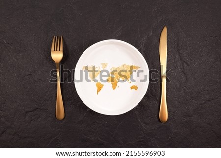 Bread in shape world map on white plate. Gold fork and knife on a dark stone background. Abstract Concept of global hunger.