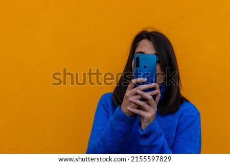 Close-up portrait of pretty young girl using mobile taking pictures snap isolated over orange color background