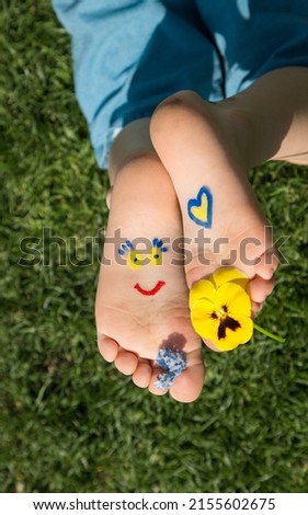 smiling face and heart are painted on children's bare feet in yellow and blue. Children against war. positive atmosphere, hello summer. attracting attention of world community to problem of Ukraine