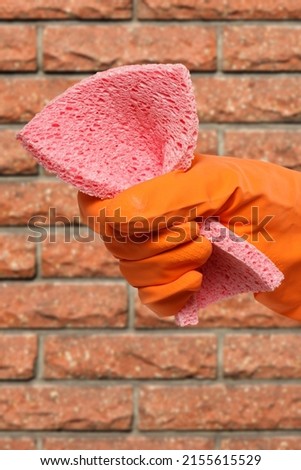 Close-up view of woman's hand in rubber protective glove with a sponge and a brick wall on the background. Cleaning concept.