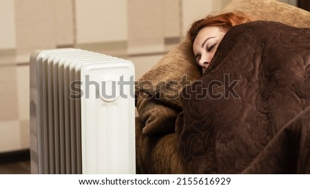 A young girl sleeps wrapped in a blanket near the heating radiator at home. Heating season. Royalty-Free Stock Photo #2155616929