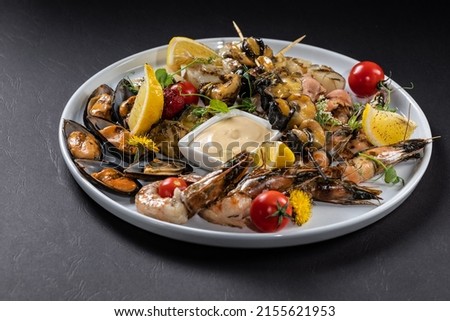 Set of seafood from mussels, shrimps, scallops and rapans with lemon and tomatoes on a white plate. Black background Royalty-Free Stock Photo #2155621953