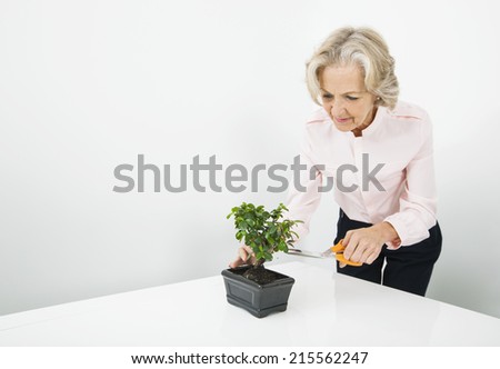 Senior businesswoman pruning plant at desk in office