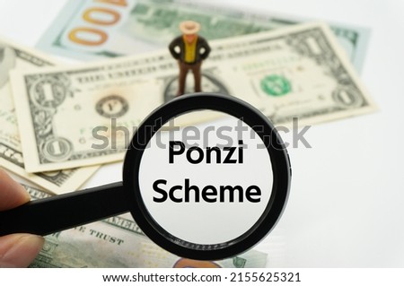 Ponzi Scheme.Magnifying glass showing the words.Background of banknotes and coins.basic concepts of finance.Business theme.Financial terms. Royalty-Free Stock Photo #2155625321