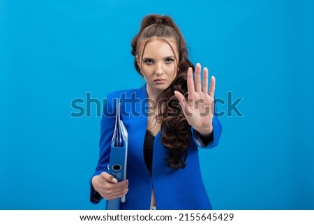 Stop sign, hand on camera, symbol - do not move. Close up photo of young serious woman shows hand right to camera, isolated on blue background. The end of stress bullying at work.