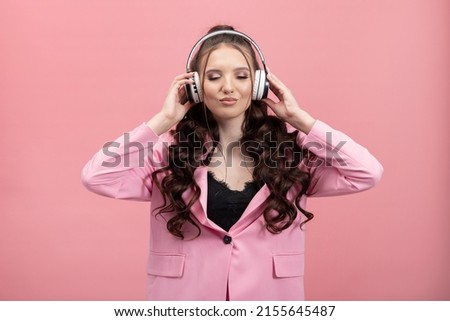 Happy young brunette woman girl in pink jacket posing on pastel background wall studio portrait. People lifestyle concept. Listening to music with headphones, dancing.