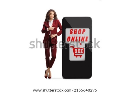 Full length portrait of a young professional woman leaning on a big mobile phone with text shop online and pointing isolated on white background