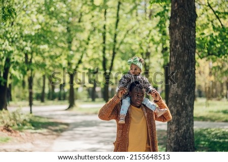 Little african american baby girl playing with her father in the park and spending great time together and having fun. Dad holding his daughter on his shoulders .