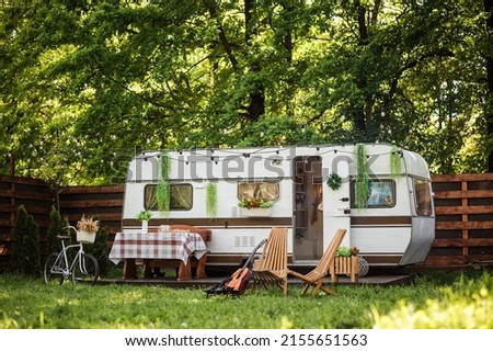 Wooden table and chairs near the trailer. Camping season. Photo studio. Trailer on the background of the forest. Bicycle on the background of the trailer