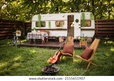 Camping season. Photo studio. Trailer on the background of the forest. Bonfire near the campsite, rest.