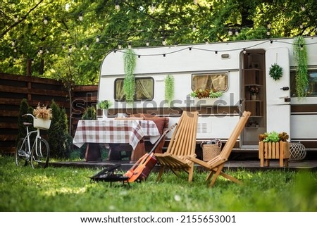 Camping season. Photo studio. Trailer on the background of the forest. Bonfire near the campsite, rest. Bicycle on the background of the trailer. Summer, green grass.