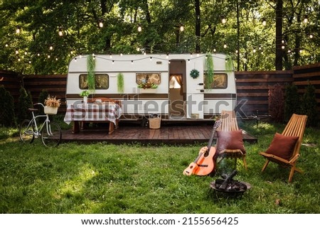 Camping season. Photo studio. Bicycle on the background of the trailer. Wooden chairs and a fire burns near them. Summer, green grass.