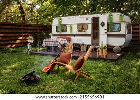 Camping season. Photo studio. Bicycle on the background of the trailer. Wooden chairs and a fire burns near them. Summer, green grass, recreation for people.