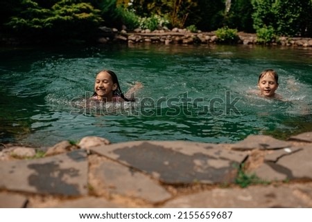 Little boy and girl are swimming in the pond on a sunny hot day. Children spend their free time relaxing outdoors. Beautiful emerald water. Summer holidays. Royalty-Free Stock Photo #2155659687