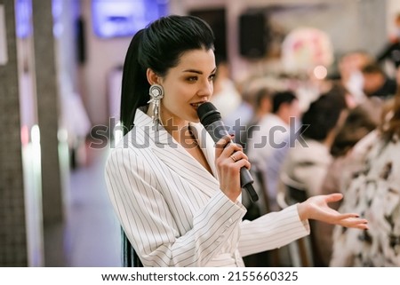Smiling brunette in a white suit. Festive mood. The girl speaks into the microphone. Host at the festival