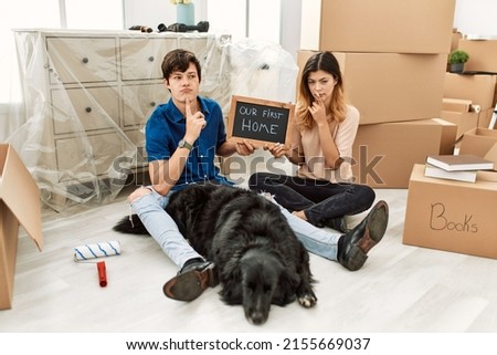 Young caucasian couple with dog holding our first home blackboard at new house thinking concentrated about doubt with finger on chin and looking up wondering 