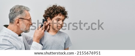 Positive curly male child while ear examining with audiologist. ENT doctor checking boy ear using otoscope Royalty-Free Stock Photo #2155676951