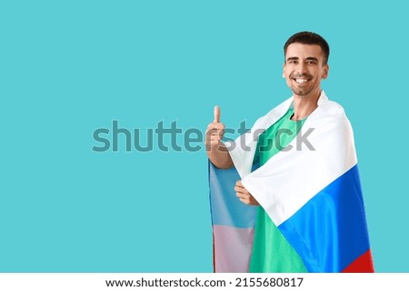 Happy young man with national flag of Russia showing thumb-up gesture on color background