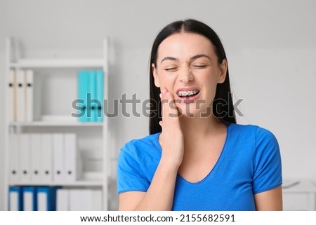 Beautiful woman with dental braces having pain in clinic