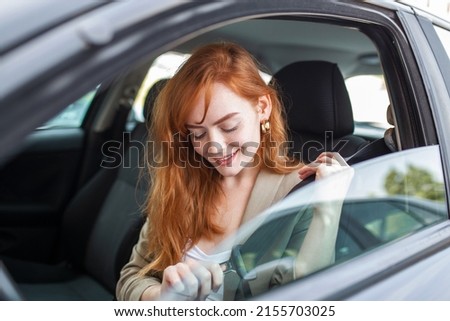 Young woman sitting on car seat and fastening seat belt, car safety concept. Woman fastens a seat belt in the car. Caucasian woman driver fastening seat belt while sitting behind the wheel car. Royalty-Free Stock Photo #2155703025