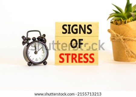 Signs of stress symbol. Concept words Signs of stress on wooden blocks. Black alarm clock. Beautiful white table white background. Psychological business and signs of stress concept. Copy space.