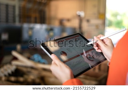 Action of a working is using tablet to review factory report with blurred background of warehouse. Business management and technology concept photo. Close-up and selective focus at human's hand part. Royalty-Free Stock Photo #2155722529