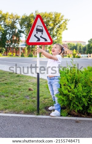 a little child girl stands with a road sign slippery road, the concept of traffic rules