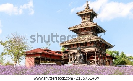Landscape shot of traditional Nepalese style pavilion temple with buddha statue overlooking field of purple violet pink flowers Royalty-Free Stock Photo #2155751439