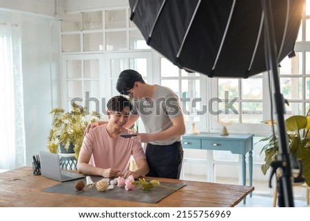 Young smiling gay couple working on new project and shooting pictures of new product by smartphone